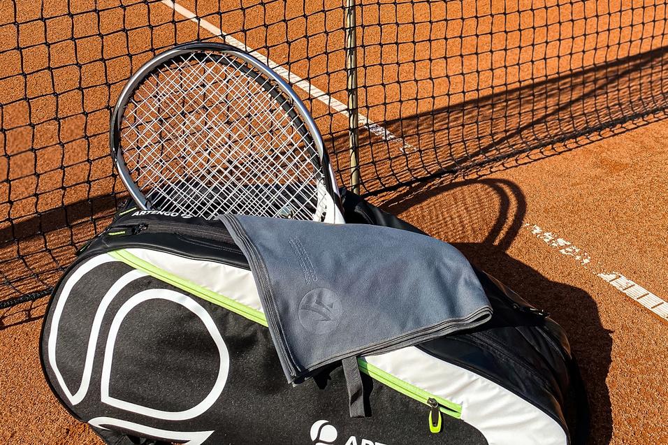 Tennisplatz mit Netz, einer ARTENGO-Tasche und einem Schläger im Vordergrund auf dem rotem Sand.